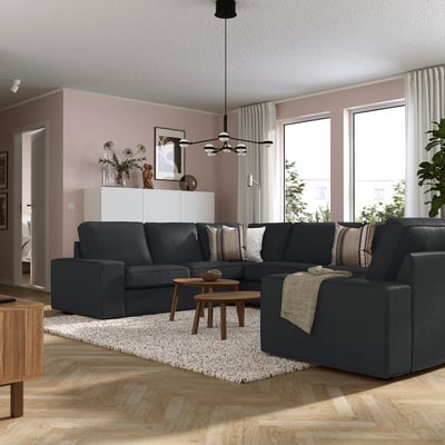 Moderne woonkamer met KIVIK grijze bank, houten tafels, roze muren, grote ramen en witte gordijnen.