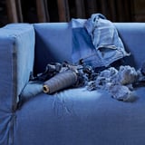 Blauwe denim bankhoes met losse draden en jasje, met versleten jeans die is omgebouwd tot meubels.