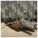 Houten hulpmiddel met grijze string op beige doek, achtergrond heeft grijze geweven muur met hangende strings.
