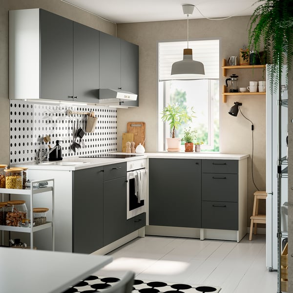 L-vormige grijze keuken: donkere kasten, marmeren toonbank, licht, plant, open planken, houten kruk.