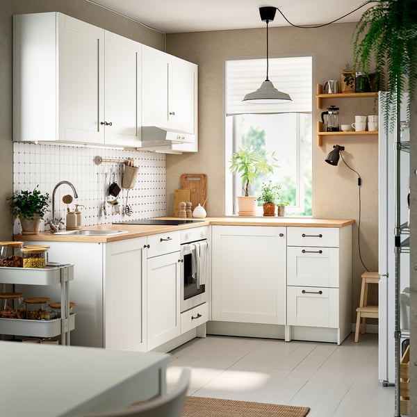 Kleine, witte, l-vormige keuken met eiken aanrechtblad, planten en hanglamp.