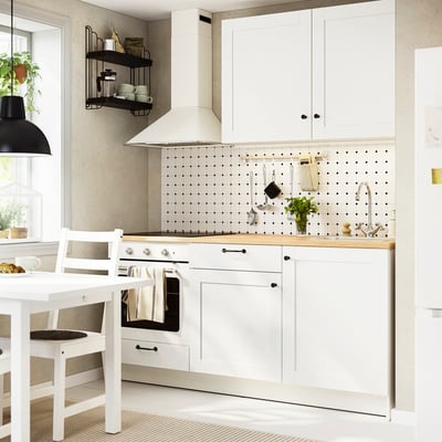 Moderne keuken met eiken aanrecht, hangpotten en planten. Witte kasten, fornuis, gootsteen en eethoek.