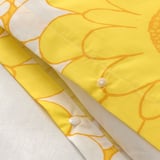 Felgele sprei met grote witte bloemen en zichtbaar stikseldetail.