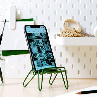 KRUBBET groene telefoonstandaard op bureau met touwen, kleine voorwerpen, potlood en potten.