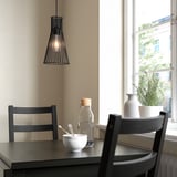 Boven een donkerhouten tafel hangt een kleine hanglamp van zwart draad naast twee donkerhouten stoelen bij een raam met een wit frame.