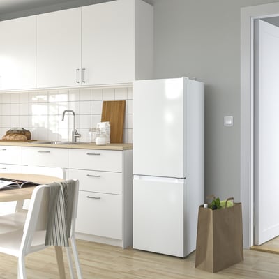 Moderne witte LAGAN koelkast in de keuken, hoog met led-licht, naast kasten en stoelen.