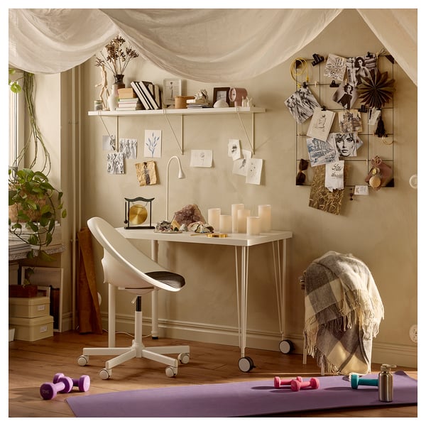 Gezellig thuiskantoor met wit LAGKAPTEN bureau, stoel en versierde muur. Plank met boeken, planten en kaarsen. Yogamat en halters op de vloer.
