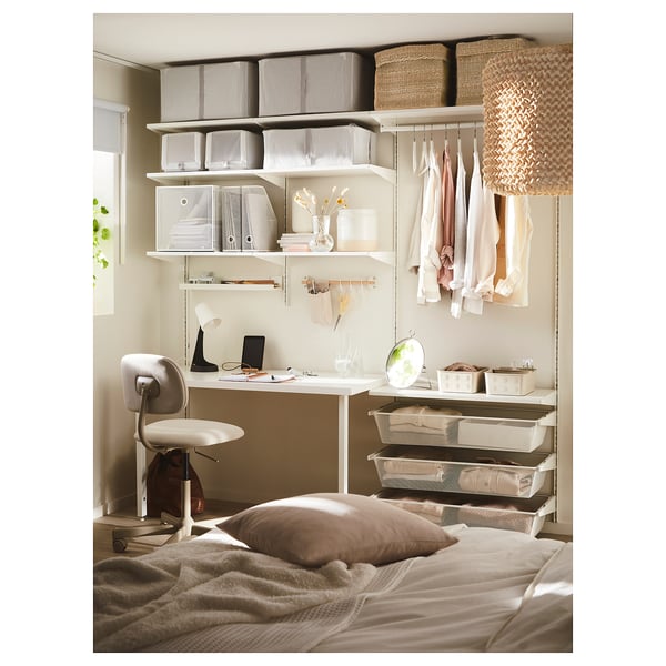 Klein kantoor aan huis in de slaapkamer. Bureau met stoel, planken, manden en lamp. Beige en witte inrichting.