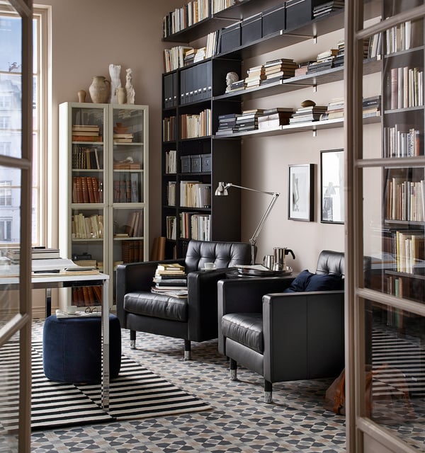 Bibliotheekkamer met LANDSKRONA zwarte leren stoelen, zwarte boekenplanken en tapijt met patronen.