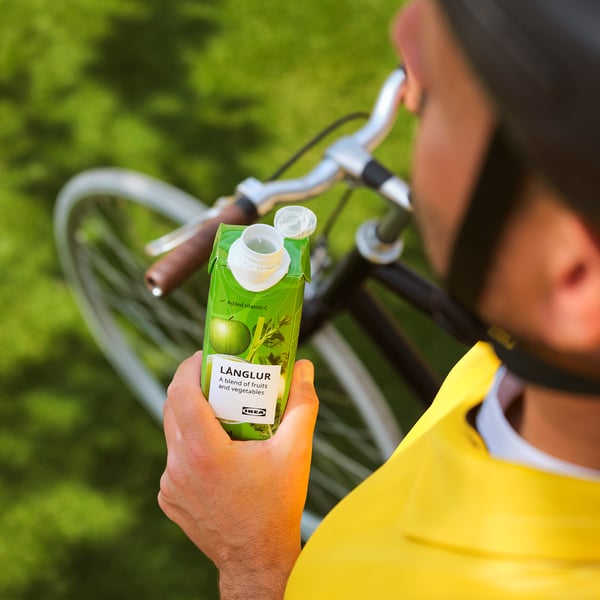 Een persoon houdt een groene LÅNGLUR-smoothie vast en toont het etiket terwijl hij buiten op de fiets zit.