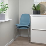 Twee gestapelde blauwe stoelen onder een raam met planten.