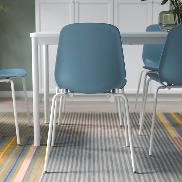 Drie blauwe stoelen met witte metalen poten staan rond een witte tafel op een gestreept vloerkleed, ideaal voor flexibel zitten en eenvoudig schoonmaken.