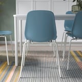 Drie blauwe stoelen met witte metalen poten staan rond een witte tafel op een gestreept vloerkleed, ideaal voor flexibel zitten en eenvoudig schoonmaken.