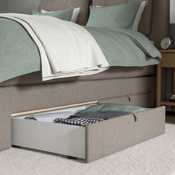 Opberglade onder het bed van de LILLFJÄLLET boxspring, met opgevouwen dekens en beddengoed.