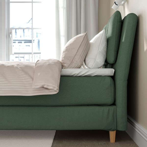 Groene boxspring met kussens bij het raam, voor comfort en stijl.