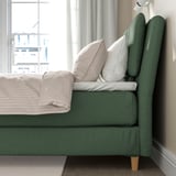 Groene boxspring met kussens bij het raam, voor comfort en stijl.