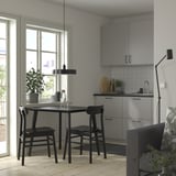 Moderne keukenhoek met LISABO zwarte tafel, stoelen met houten poten, grijze kasten, witte achterwand, planten en hanglamp.