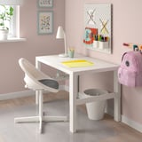 Eenvoudige opstelling van een wit kinderbureau. Klein wit bureau met stoel, prullenbak, lamp en wanddecoraties.