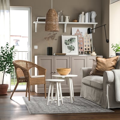 Moderne woonkamer met grijze bank, witte tafels, een rotan stoel en houten decoratie. Gezellige, goed verlichte, neutrale kleuren.