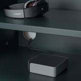Een grijze koptelefoon die op een donker oppervlak rust, aangesloten op een oplaadapparaat.