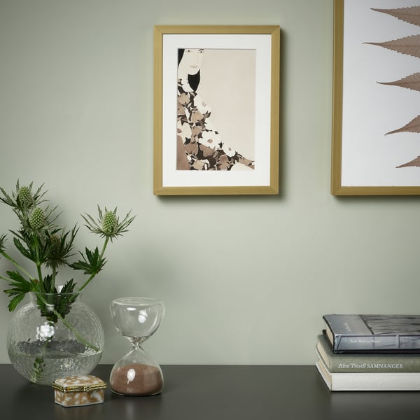 Ingelijst beeld op groene muur met vaas, zandloper, boeken op tafel