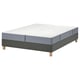 Een geassembleerd bed met een witte en grijze matras op een grijze basis met houten poten.