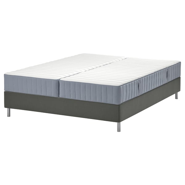 Afbeelding toont een gespleten, tweekleurige kingsize matras op een donkergrijze platformbodem. De basis heeft metalen poten en een eenvoudig ontwerp.