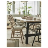 Lichte eethoek met groot raam, houten tafel, MALINDA beige stoelkussens, potplanten en zwarte metalen stoelen.