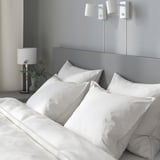 Bed met vier donzige kussens, stijlvolle lamp ernaast, twee moderne wandlampen erboven.