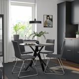 Moderne eethoek met ronde tafel en grijze stoelen, strakke poten, polyester bekleding, gezellige keukenhoek met kunst en planten.