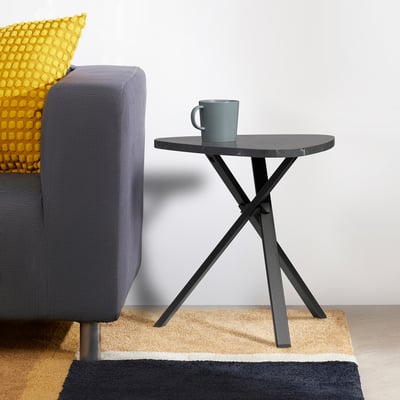 Moderne grijze bijzettafel met gekruiste poten naast een fauteuil.