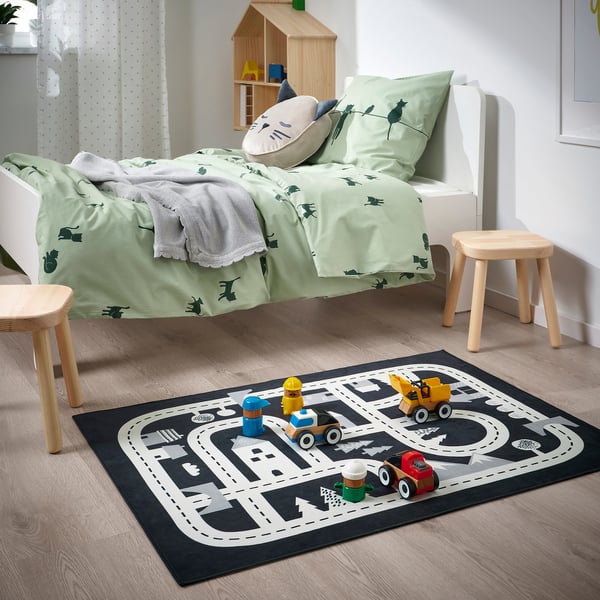 Kinderkamer met MARKKRYPARE zwart & grijs speelkleed met speelgoedvoertuigen. Vloerkleed past onder een klein bed, houten krukken in de buurt.