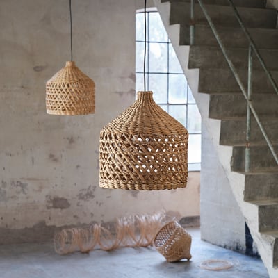 Twee MÄVINN rieten hanglampen hangen aan het plafond naast een betonnen trap, met natuurlijke vezels en een ingewikkeld geweven ontwerp.