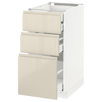 Een witte METOD keukenkast met drie beige lades met een glanzende afwerking en geïntegreerde handgrepen.