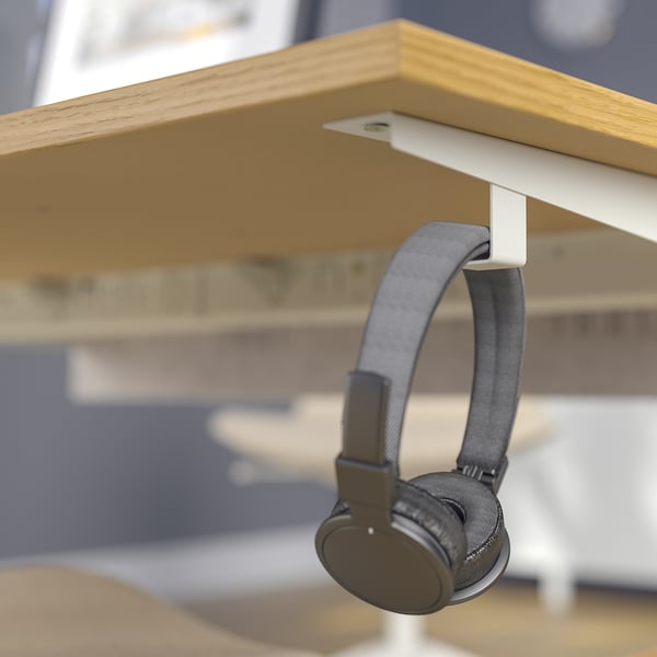 Een koptelefoon hangt aan een haak onder een houten bureau en toont het kabelbeheer en de opslag van het bureau.