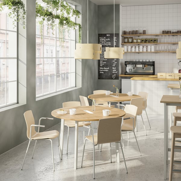 Minimalistisch café met houten tafels, lichte stoelen, planten en koffiezetapparaten.
