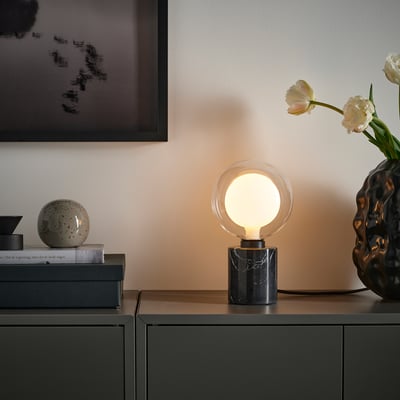 Optische godfrey tafellamp: MOLNART met marmeren voet, warm licht op plank met decor.