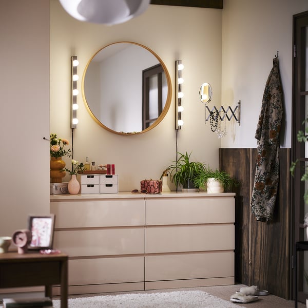 Moderne slaapkamer met wandlampen, spiegel, kist, planten en vloerkleed.