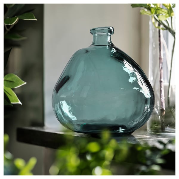 Midden: grote blauwe vaas van gerecycled glas met bubbeltextuur. Omringend groen. Tafel achtergrond.