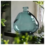 Midden: grote blauwe vaas van gerecycled glas met bubbeltextuur. Omringend groen. Tafel achtergrond.