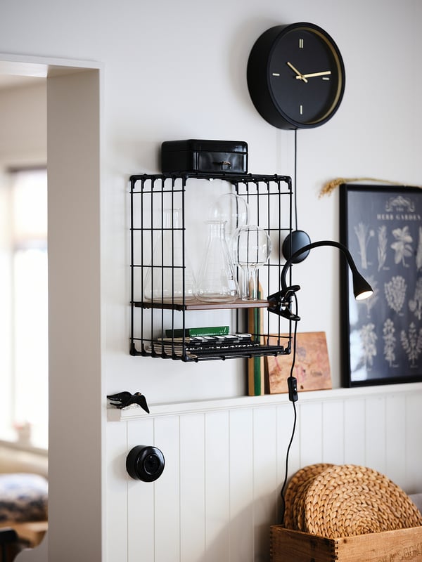 Moderne kamer met zwarte klok, glaswerkplank en klemlamp op kralenwand.