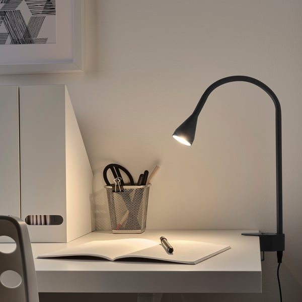 Zwarte klemschijnwerper op bureau, verlichtend boek. Regelbaar. Pennenhouder in de buurt.