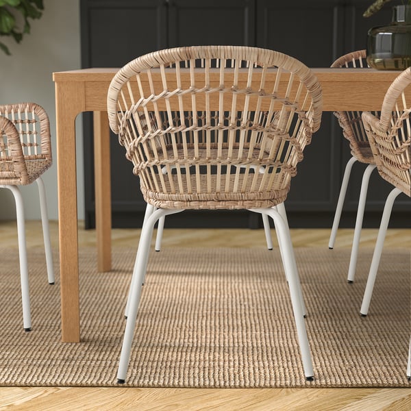 Drie gevlochten rotanstoelen met witte metalen poten rond een houten tafel op een gestructureerd tapijt. Ideaal om comfortabel te dineren.