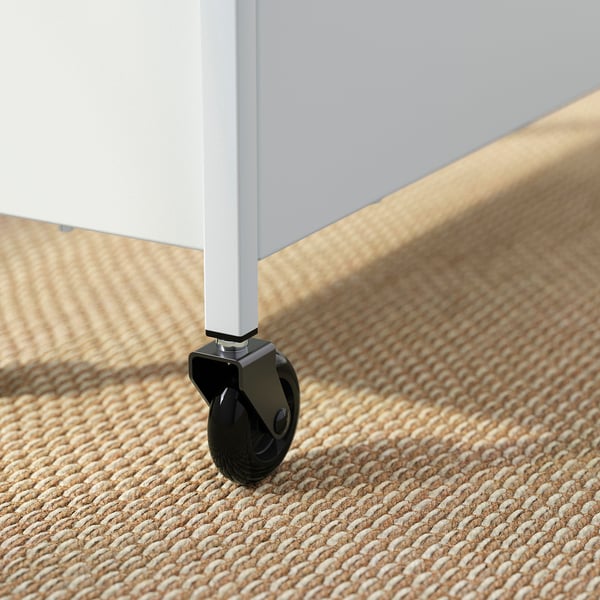Close-up van het NISSAFORS trolleywiel: stevig metalen been, gladde zwarte wiel op getextureerd beige tapijt.