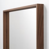 Een hoogwaardige spiegel met houten frame met strakke lijnen, gemonteerd aan een muur, die een helder en helder oppervlak weerspiegelt.