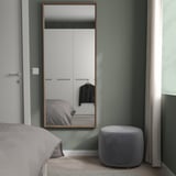 Minimalistische slaapkamer met NISSEDAL spiegel, bed, poef, gedempte groene muren, kast.