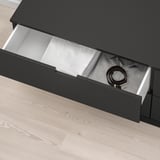 Zwarte NORDLI lade open, met riem, soft-close mechanisme zichtbaar, op lichte houten vloer.