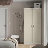 Minimalistische slaapkamer met hoge beige PAX kledingkast, kapstok en wit bed.