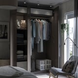 Moderne slaapkamer met PAX kledingkast, grijze planken, stoel en plant.