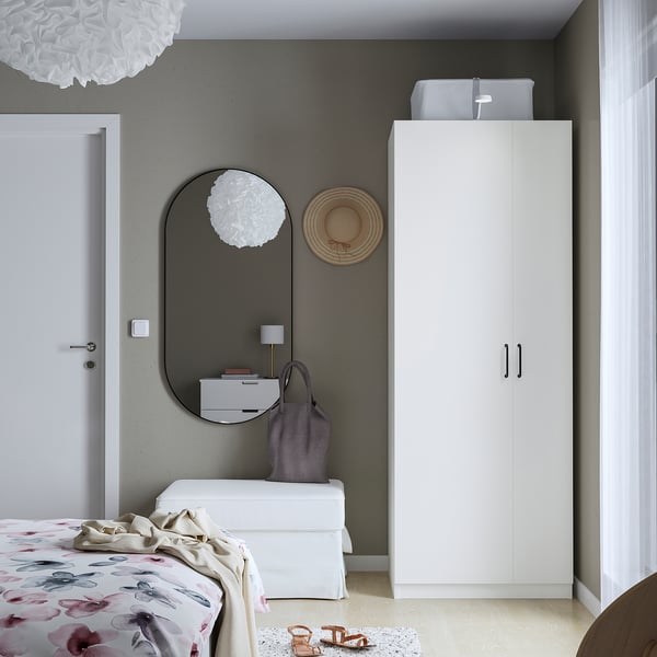 Een minimalistische slaapkamer met een hoge witte PAX kledingkast, gebloemd dekbed en spiegel.